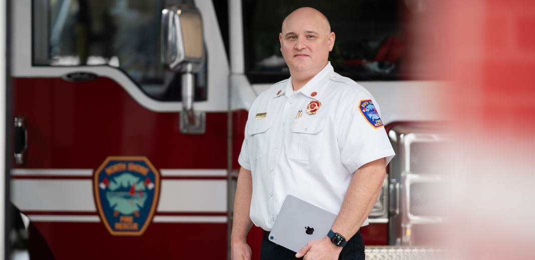The fire chief stands in front of a fire truck holding an iPad and wearing an Apple Watch